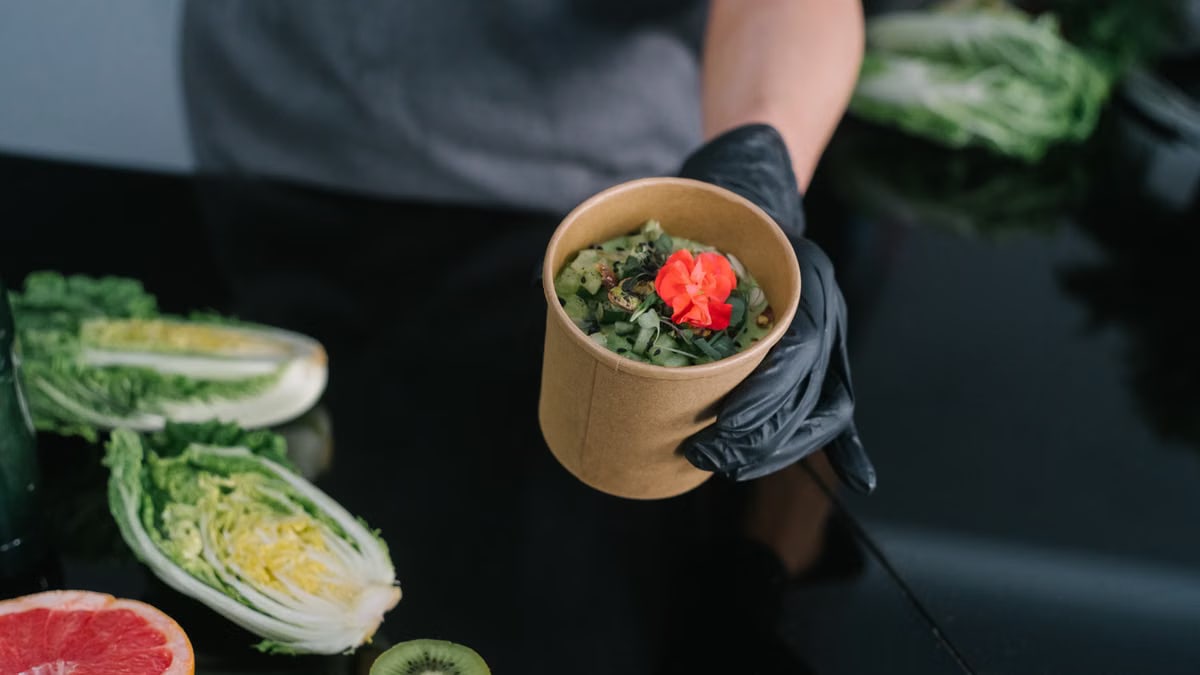 A hand holding a salad bowl with fresh vegetables and a colorful garnish, emphasizing healthy eating.