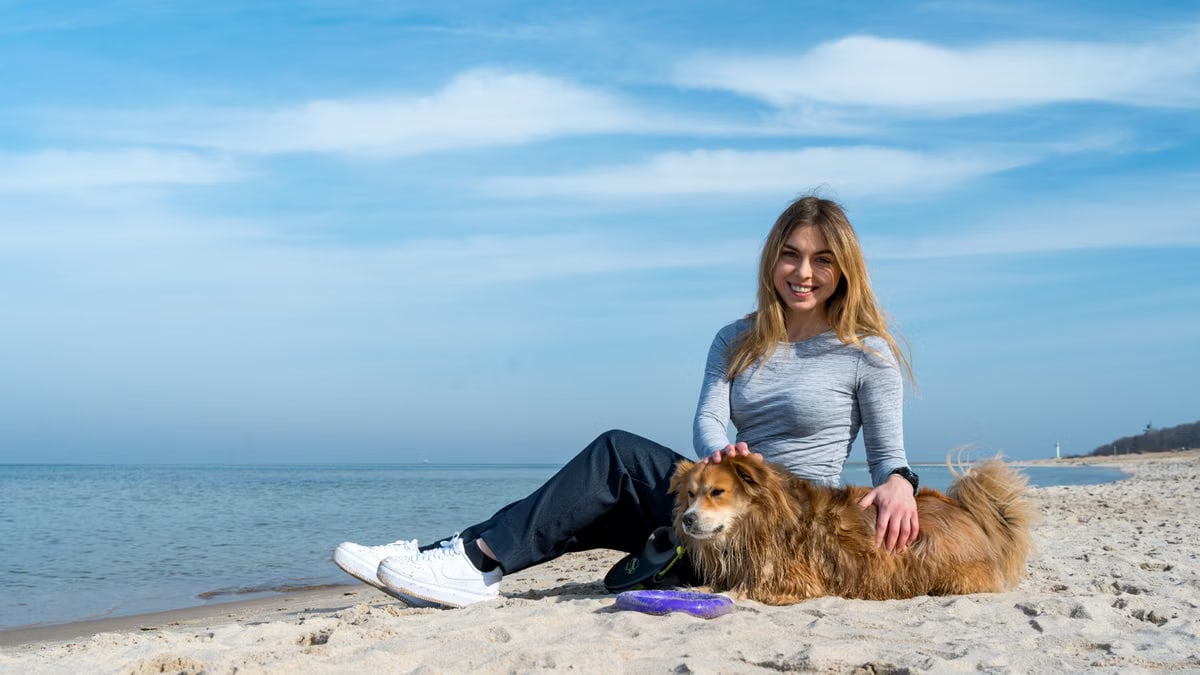 Woman enjoying a sunny day on Kołobrzeg beach with her dog, capturing the essence of leisure and companionship.
