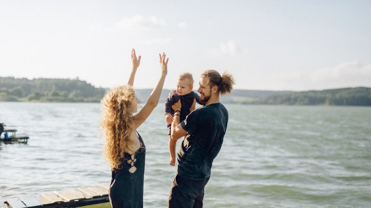 Loving family of three having fun by a lakeside on a sunny summer day.